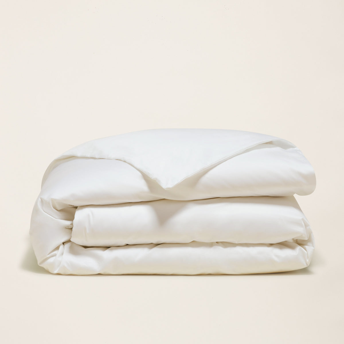 Pristine white folded duvet cover showing fluffy loft against beige background