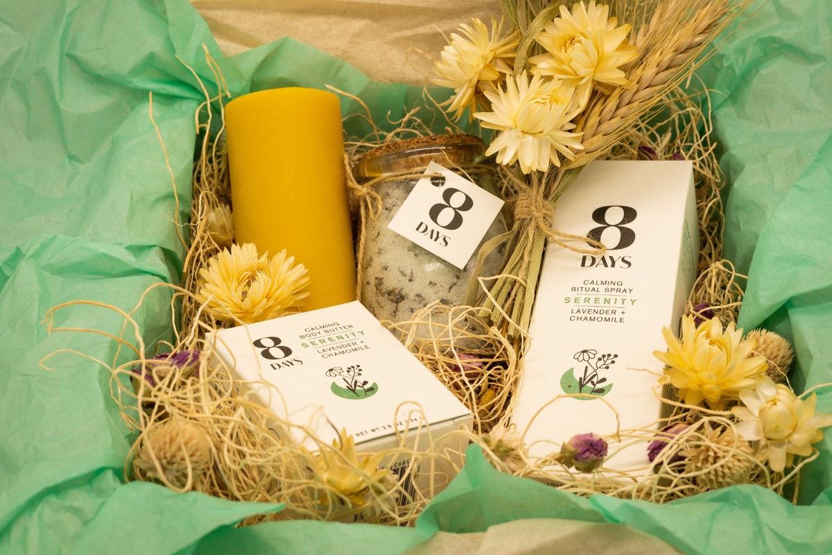 Gift set contents in mint green tissue paper highlighting speckled botanical bath salts and bright yellow strawflowers