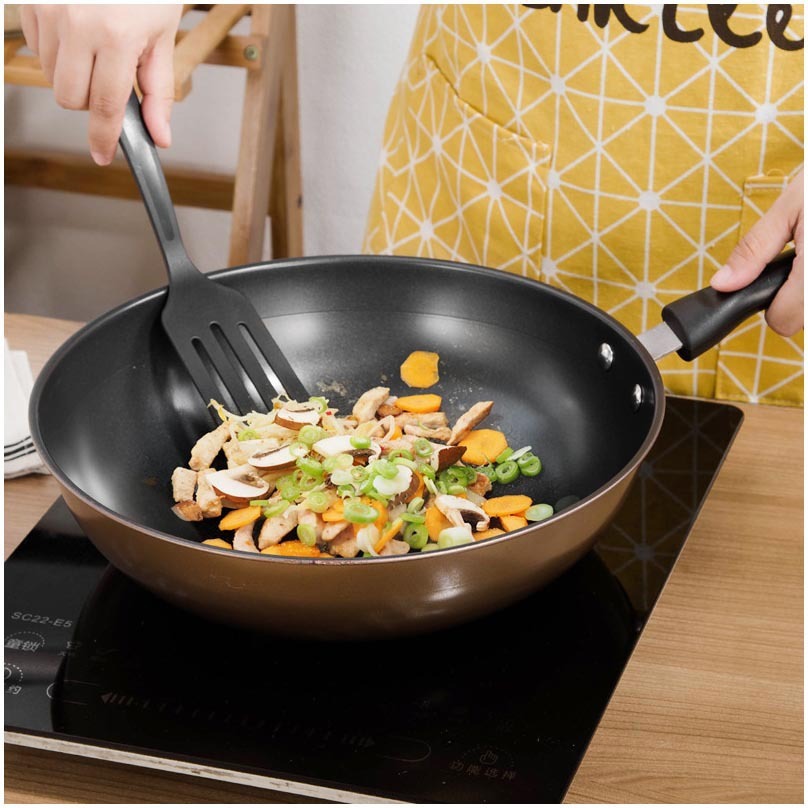 Person stir-frying vegetables in large gold wok with black non-stick interior on induction stove