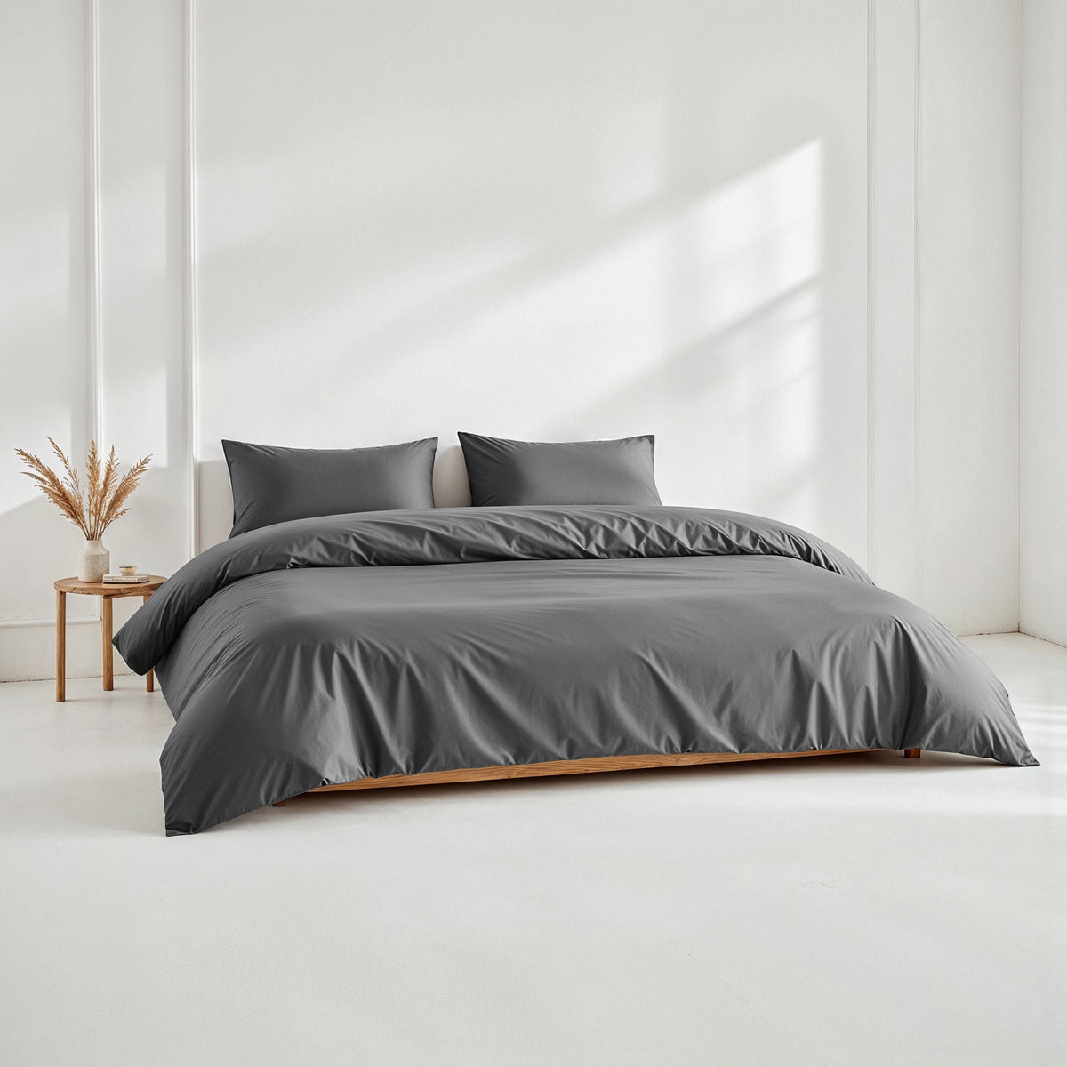 Dark charcoal grey sateen bedding set displayed on a low wooden platform bed in a bright room