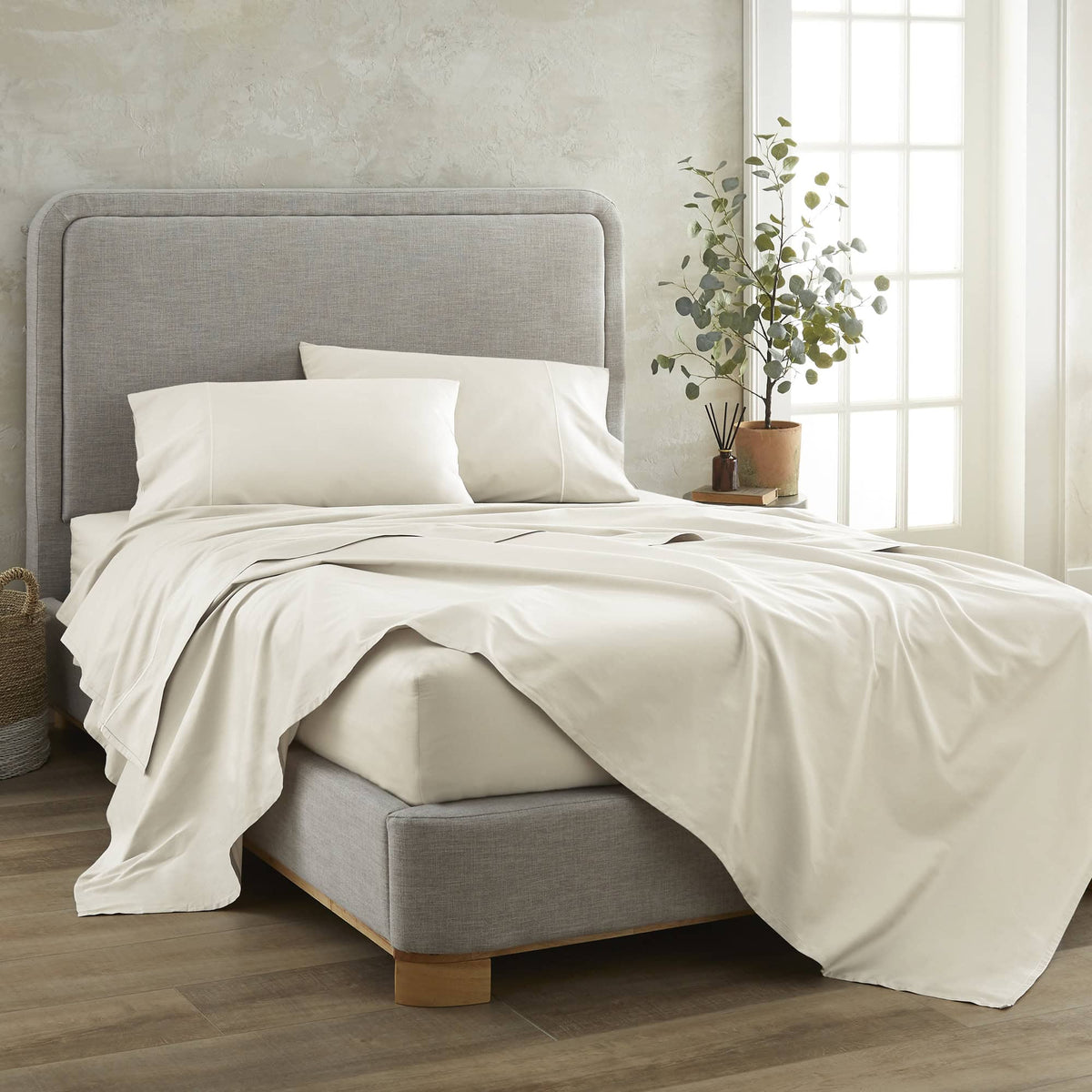 Cream organic cotton sheets cascading over grey bed frame in bright natural light