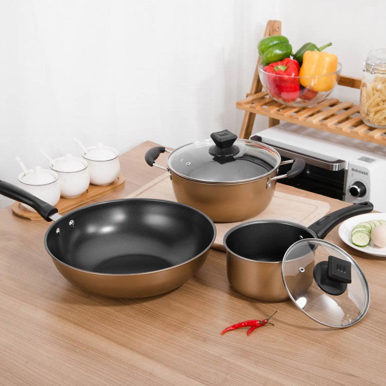 Three-piece gold cookware set with glass lids on wooden counter surrounded by fresh vegetables