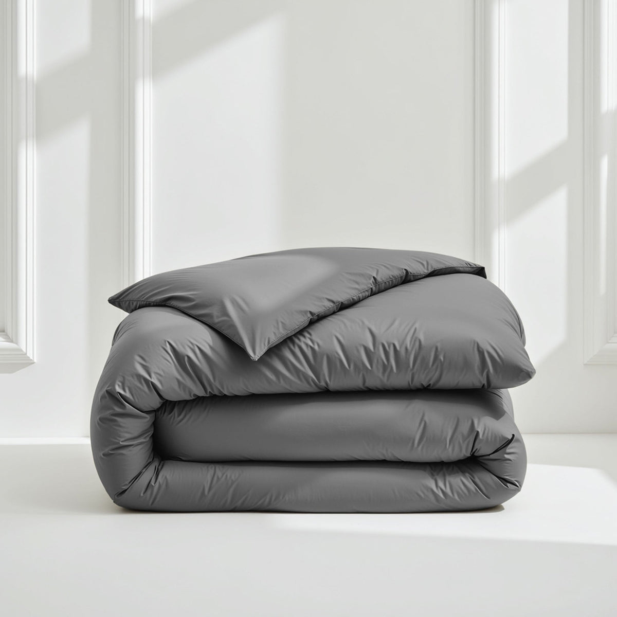 Stacked charcoal grey sateen duvet cover catching soft light on white surface
