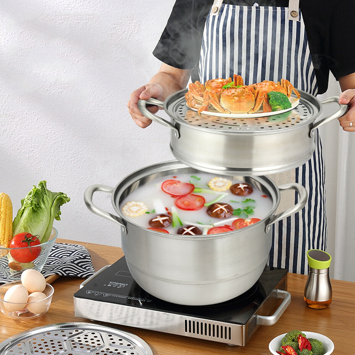 Person lifting top tier of 3 tier stainless steel steamer containing crabs and broccoli from base pot on induction cooktop
