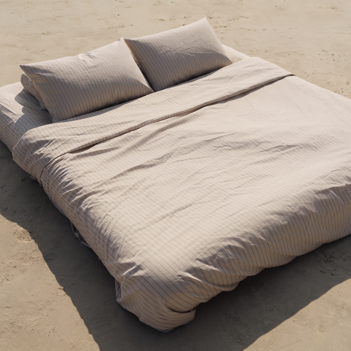 Oatmeal sateen duvet cover with thin vertical stripes draped on sandy ground in bright sunlight