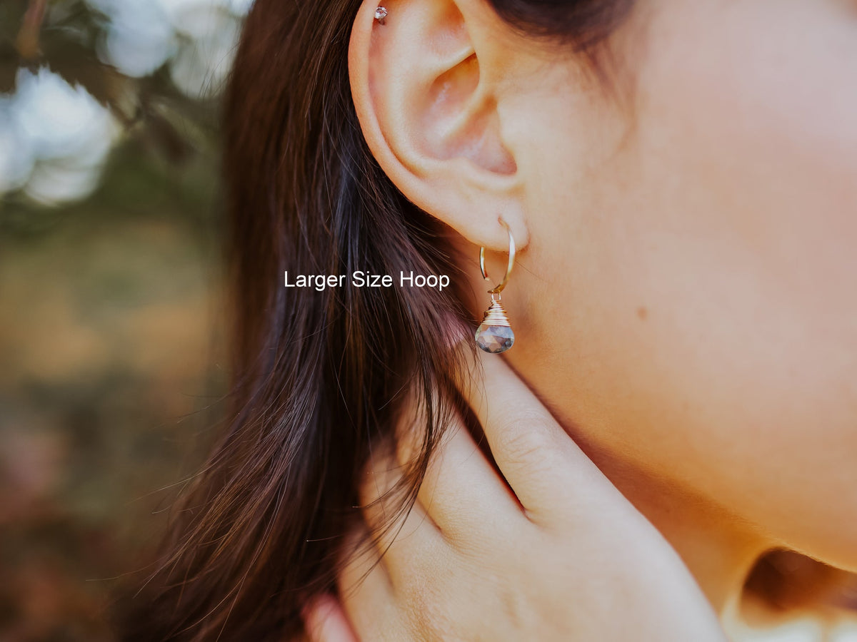 Model wearing larger gold-filled huggie earring with dangling blue-green stone