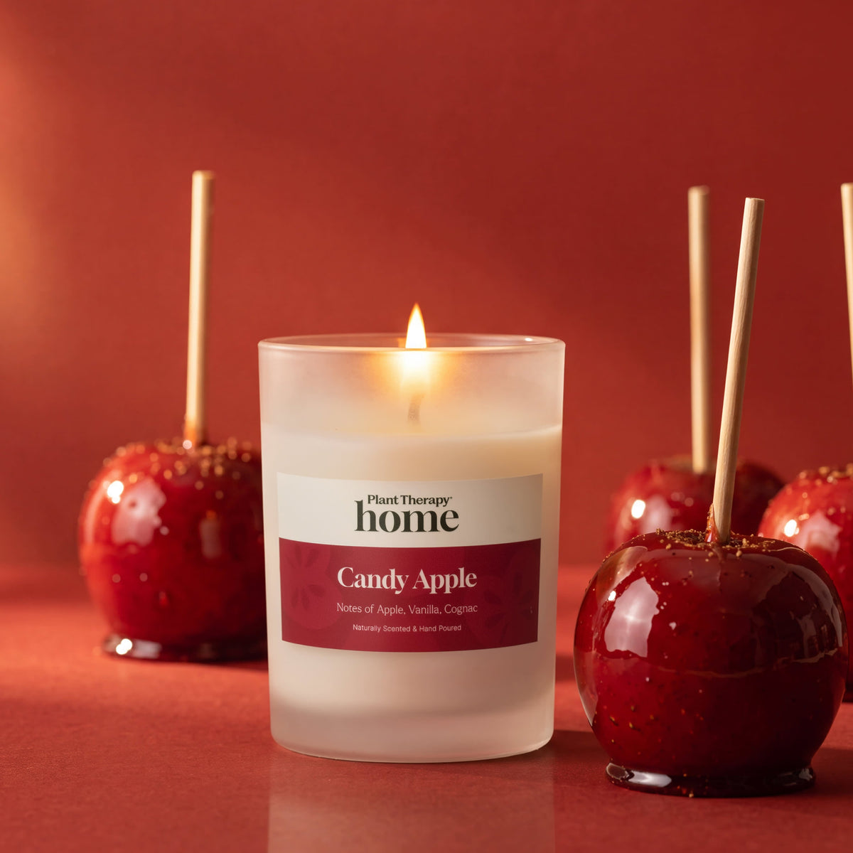 Lit candle glowing among glossy red candy apples on sticks against a rich red background