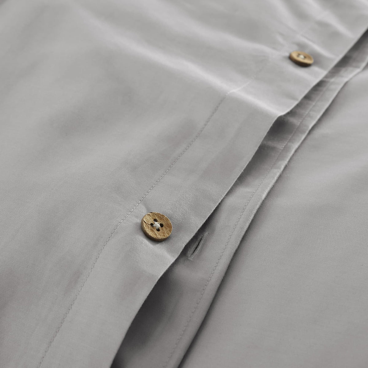 Close-up of grey duvet cover with wooden button closure and precise stitching along edge