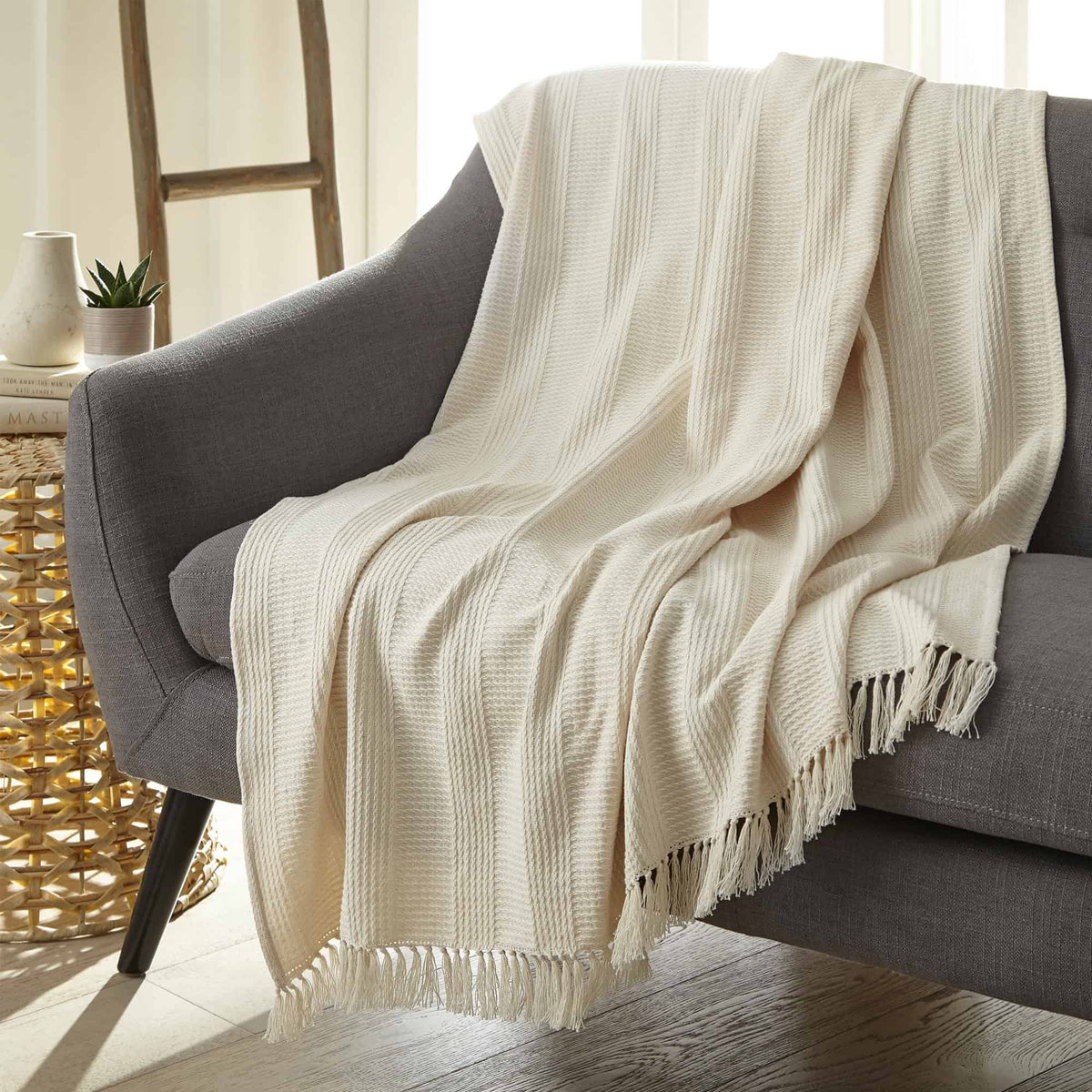 Cream waffle weave throw draped over grey armchair in sunlit room showing lightweight drape