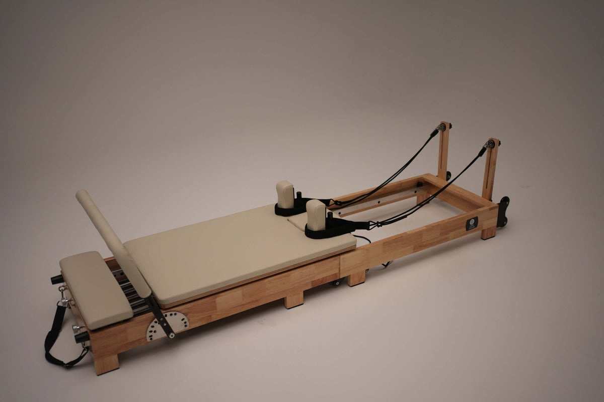 High-angle view of 90.6-inch wooden reformer frame showing sliding carriage, black rope pulley system, and adjustable footbar