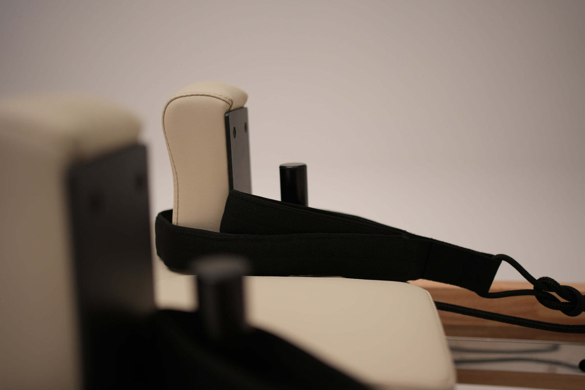 Side view focusing on black fabric straps and padded beige shoulder rests attached to the wooden reformer frame