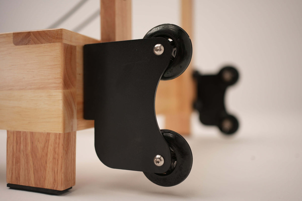 Macro shot of black metal folding mechanism with dual wheels on curved bracket attached to light wood frame for storage