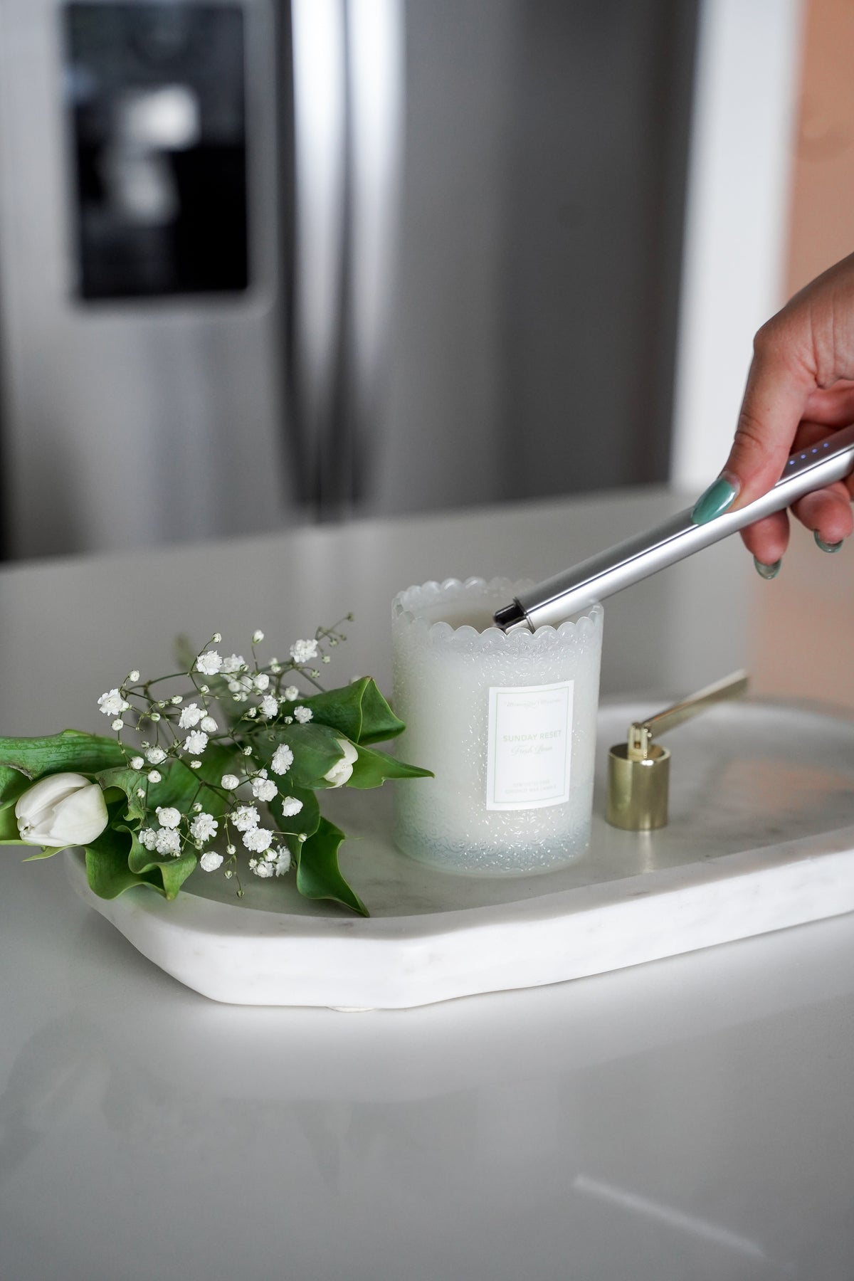 Hand lighting blue candle on marble tray with white tulips and gold snuffer nearby