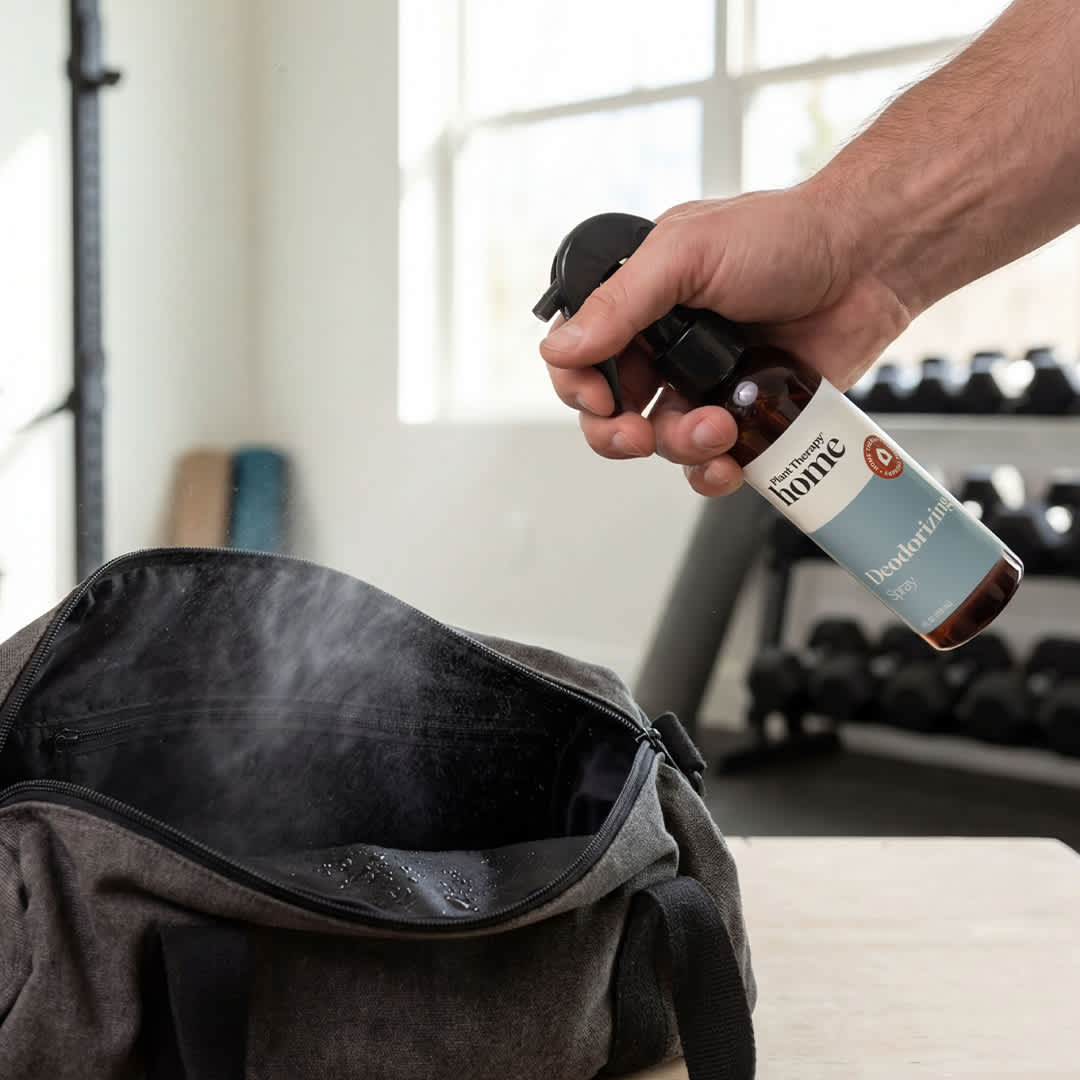 Spraying deodorizer into grey gym bag with visible droplets on black lining