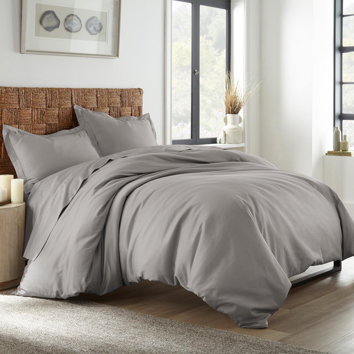 Grey sateen bedding draped on bed with rattan headboard and natural decor elements in bright room