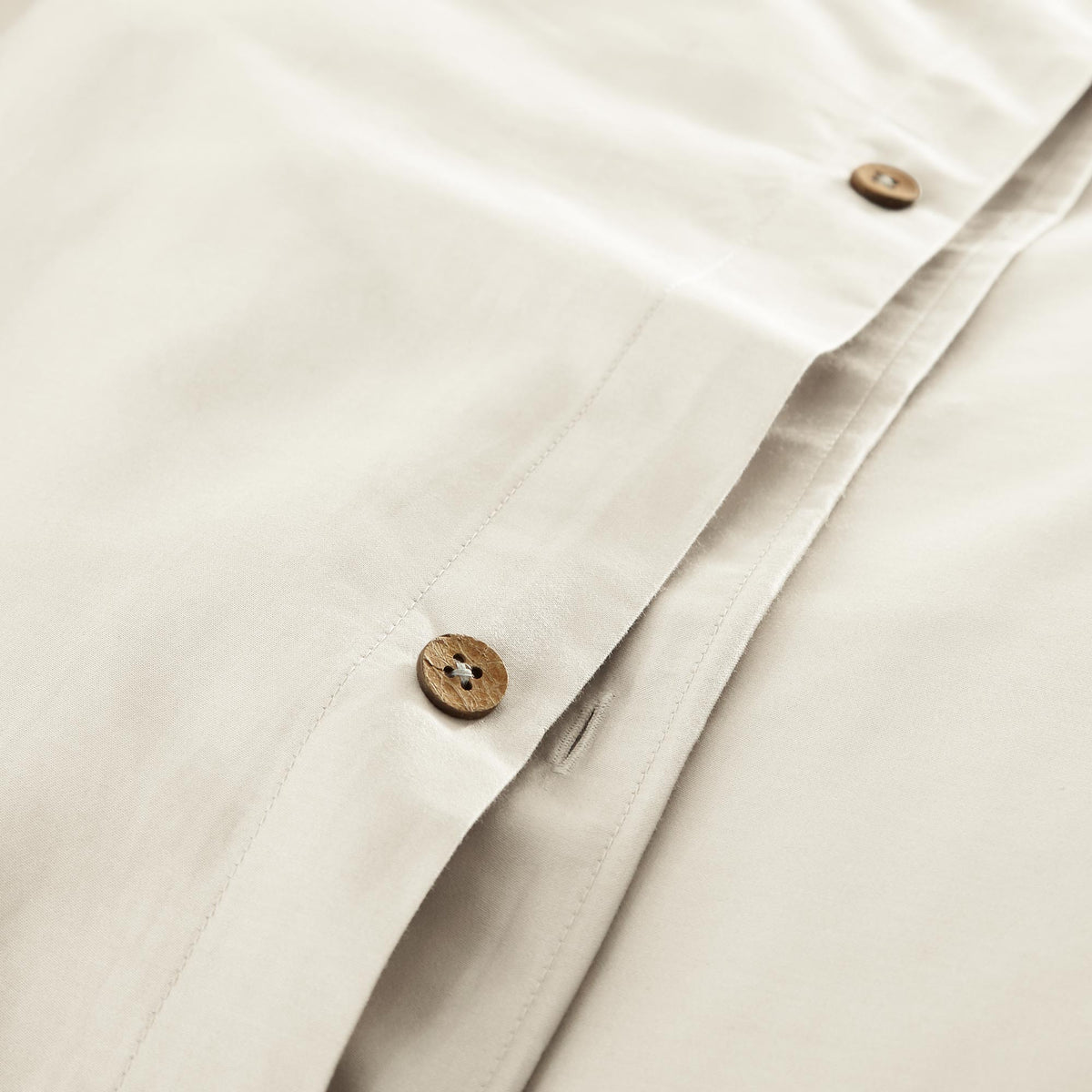 Round wooden button closure detail on cream organic cotton sateen placket with precise stitching
