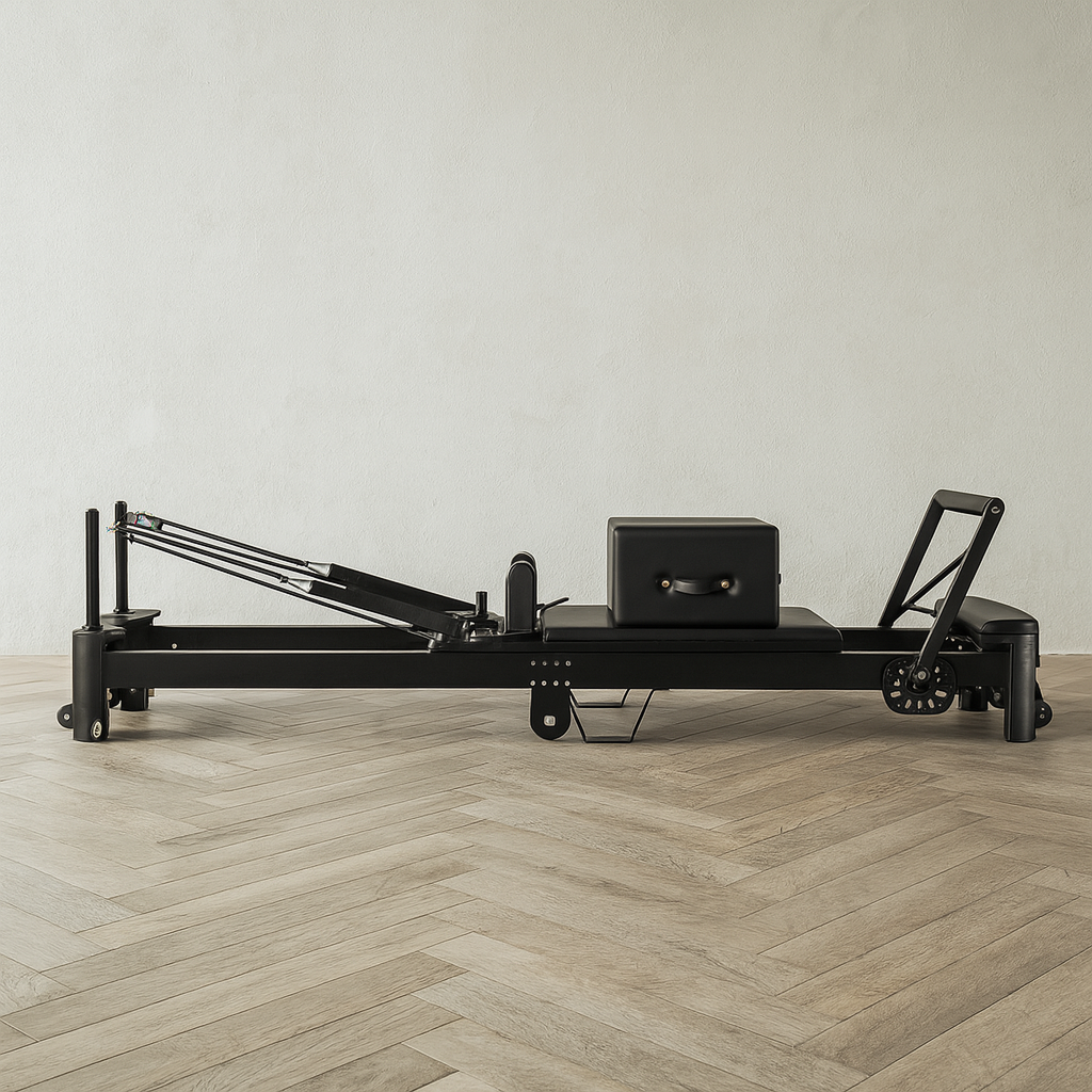 Side profile of assembled black Pilates reformer showing aluminum frame, padded carriage, adjustable headrest, and accessory