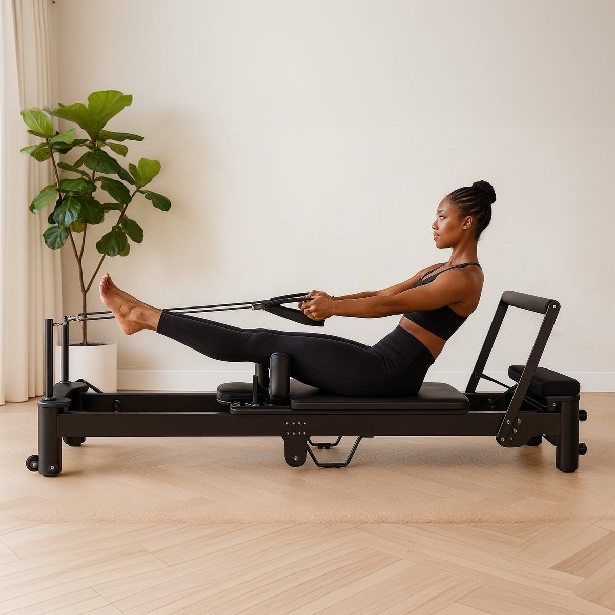 Woman in black athletic wear using a sleek black Pilates reformer with extended legs and straps on light wood flooring
