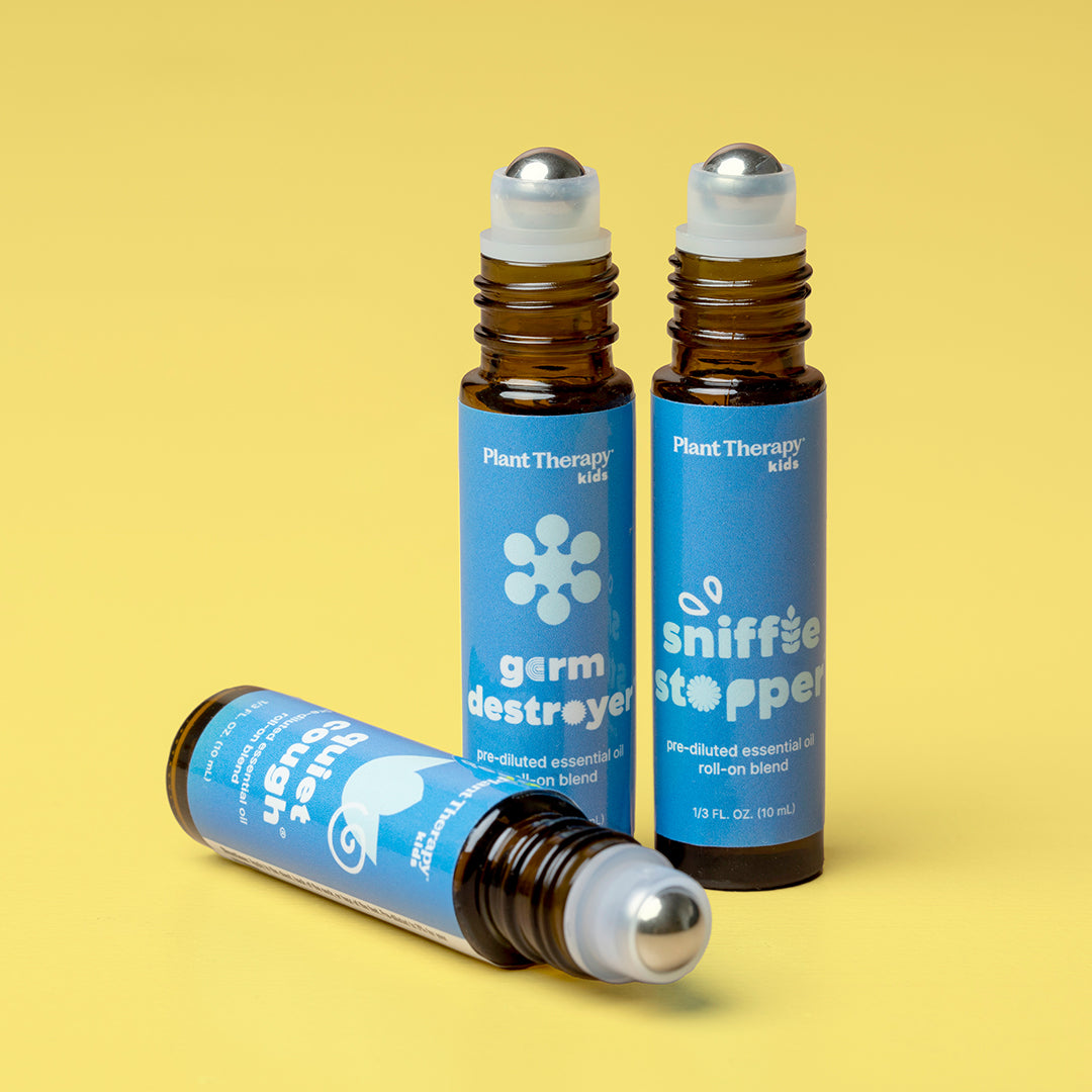 Three essential oil bottles uncapped on a yellow surface showing silver roller balls and product labels.