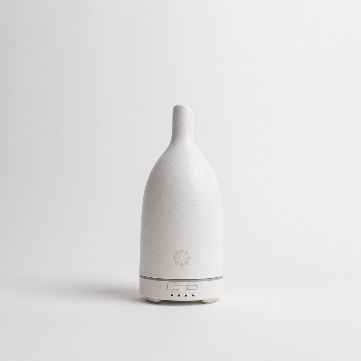 Minimalist white ultrasonic diffuser with textured body, grey base ring, and control buttons against clean background