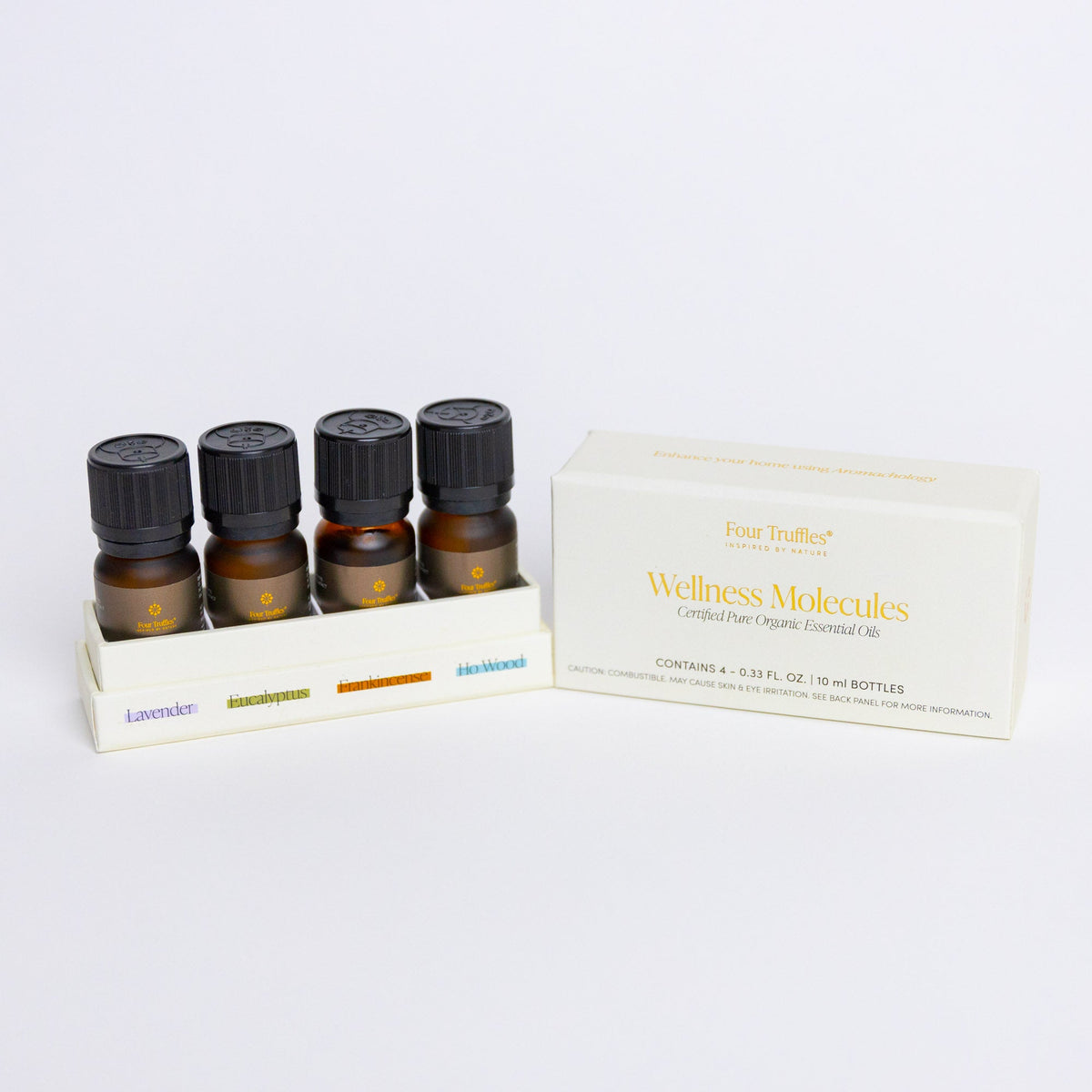 Four amber glass essential oil bottles with black ribbed caps in a white tray next to cream packaging box labeled Wellness