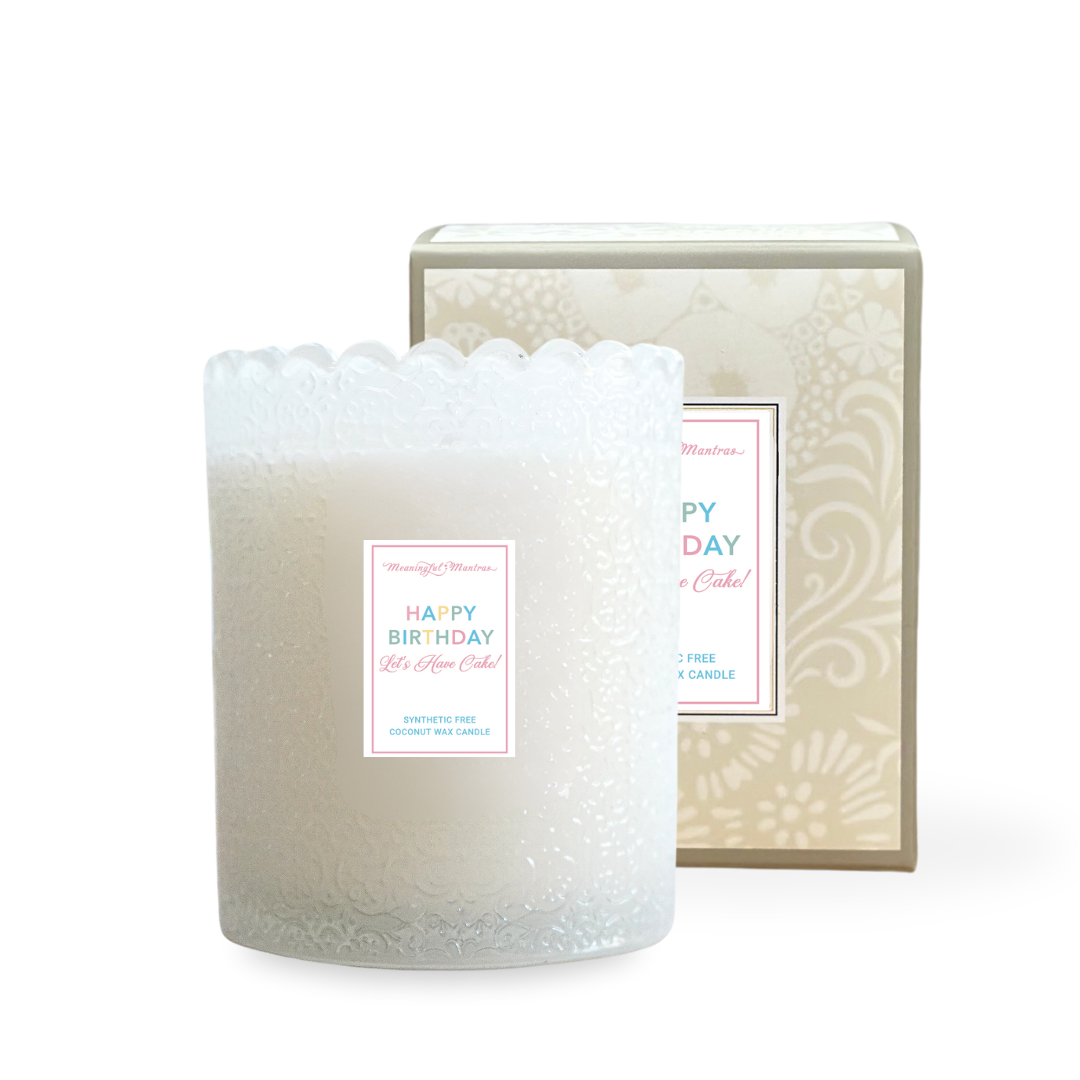 White embossed glass candle with scalloped rim sits in front of beige floral packaging box on white background