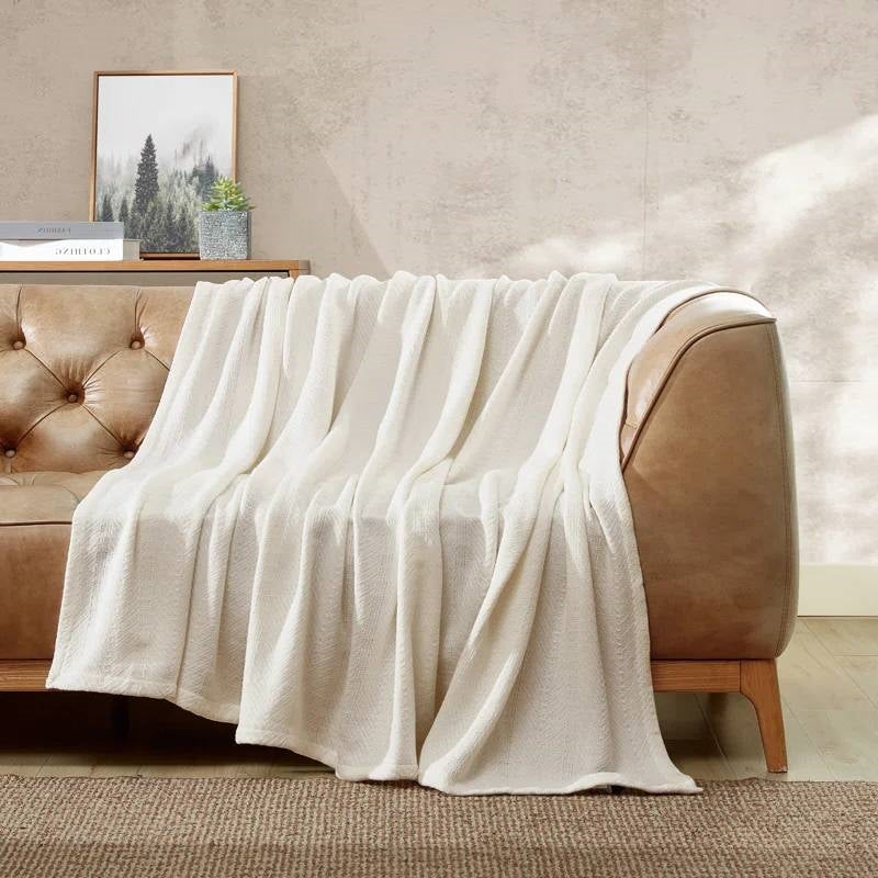 Cream bone throw blanket casually draped over a brown leather sofa in a living room setting