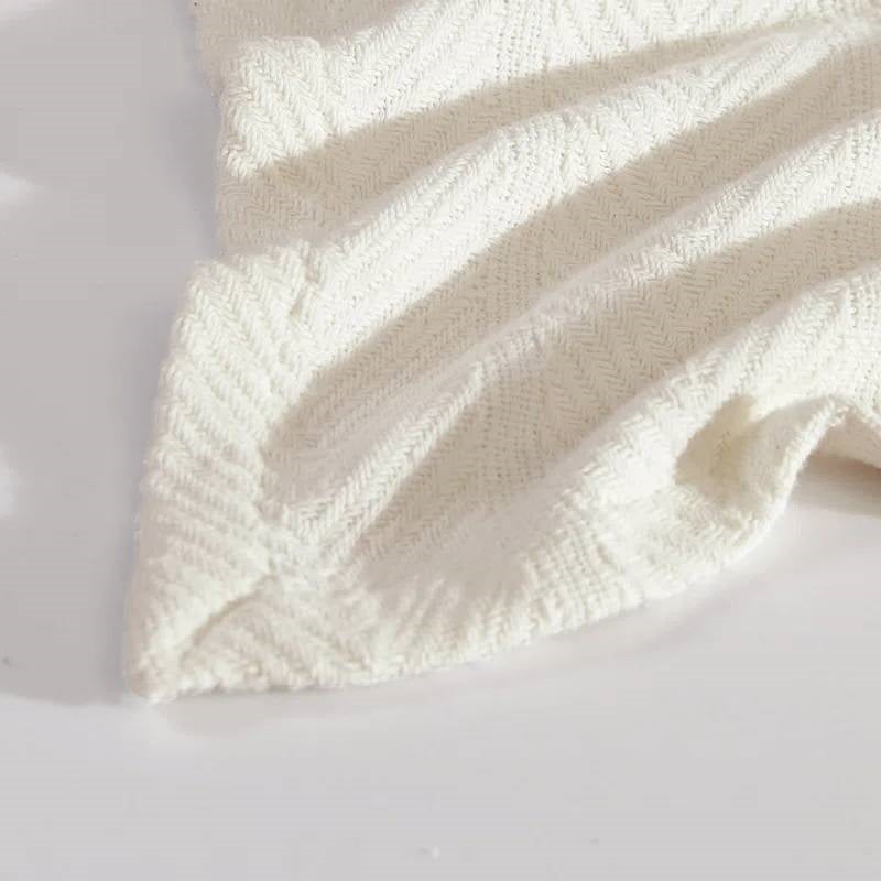 Close-up of cream bone blanket corner showing herringbone knit texture and finished hem stitching