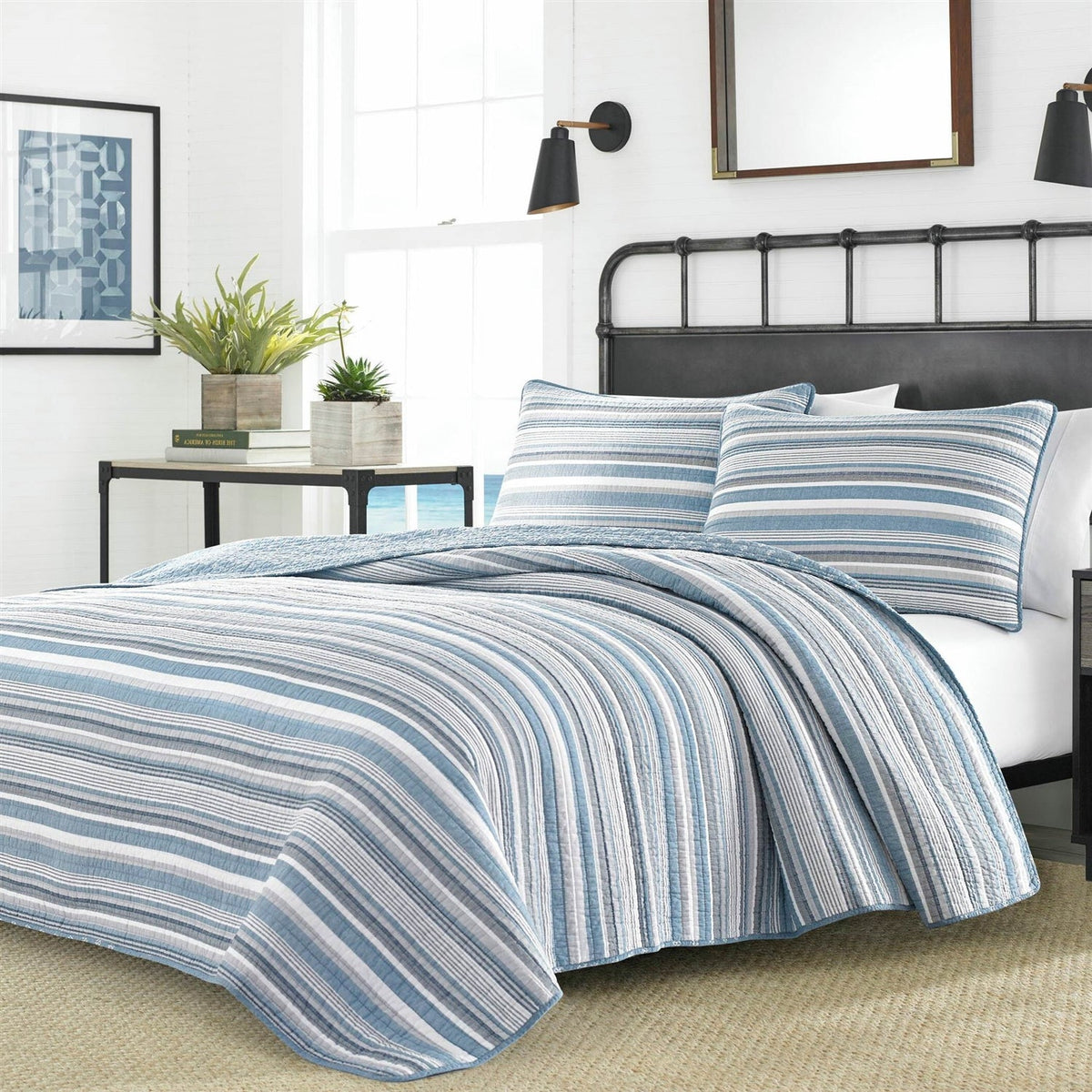 Blue white gray striped reversible quilt set on black metal bed frame in coastal bedroom