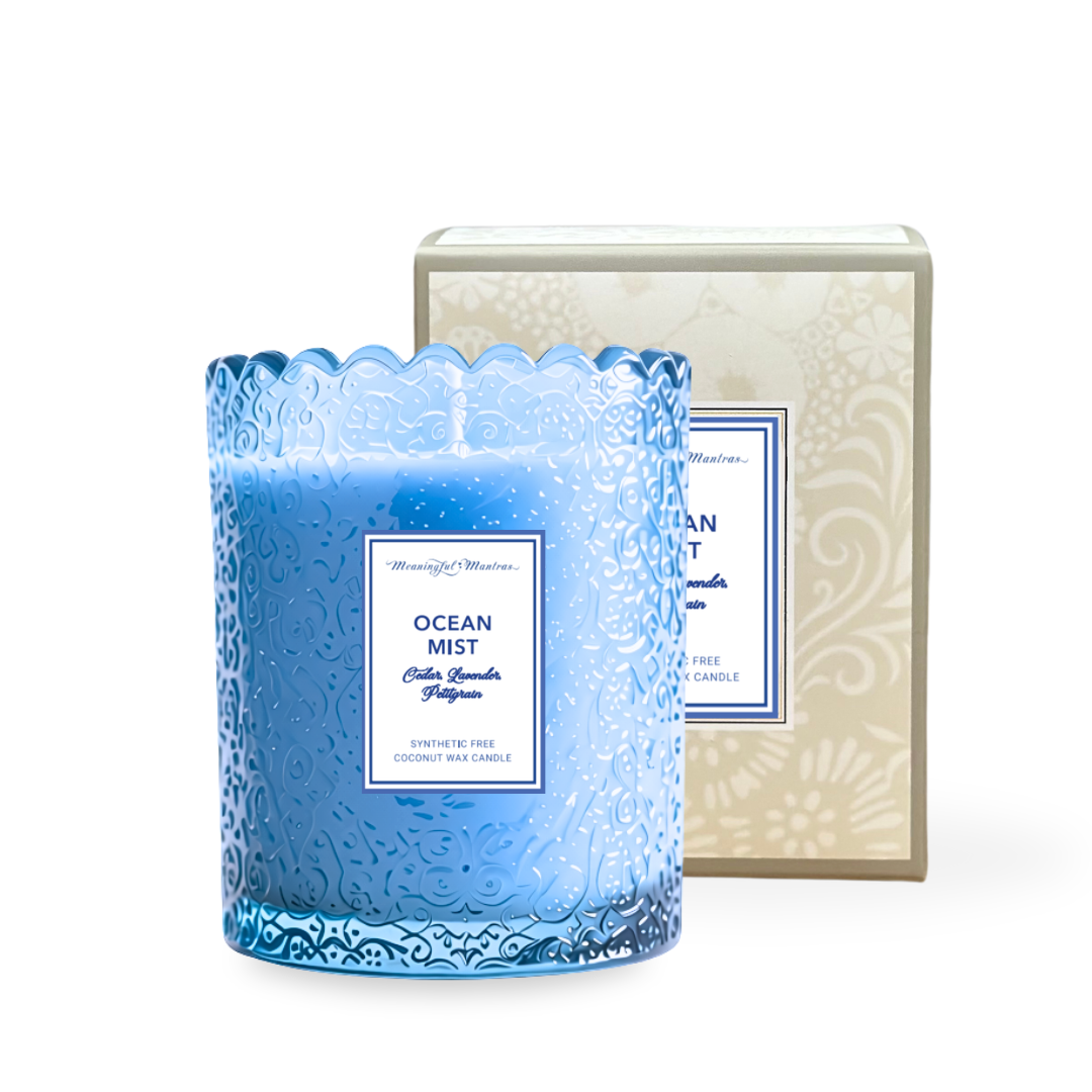 Translucent blue embossed glass candle with scalloped rim beside beige box labeled Ocean Mist