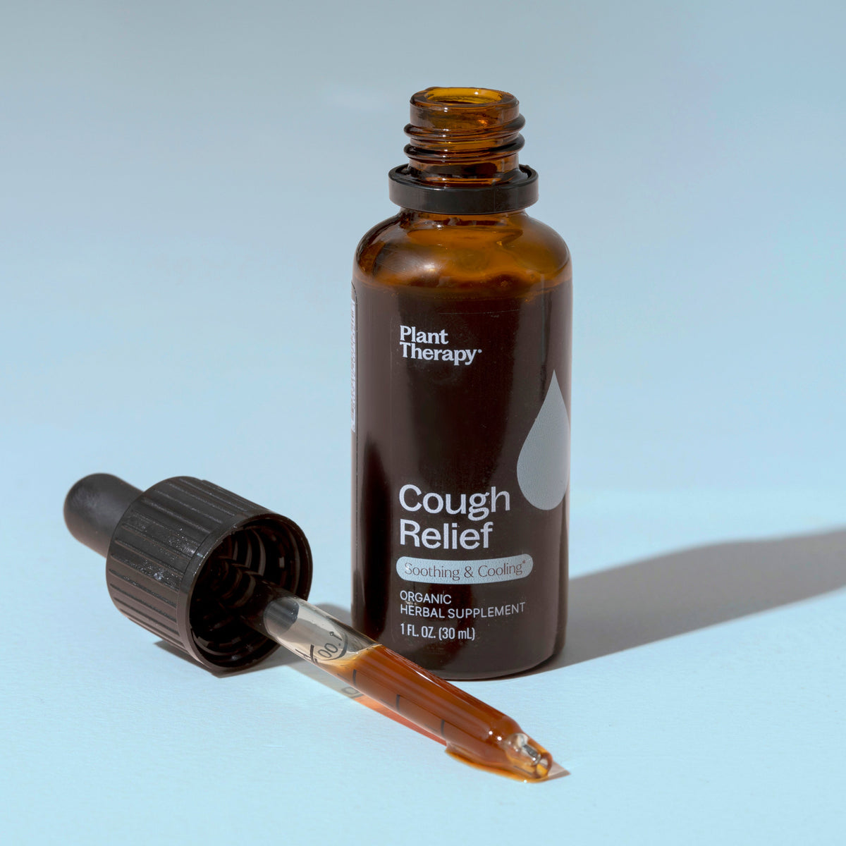 Open amber bottle standing upright next to a removed glass dropper showing amber liquid inside the pipette