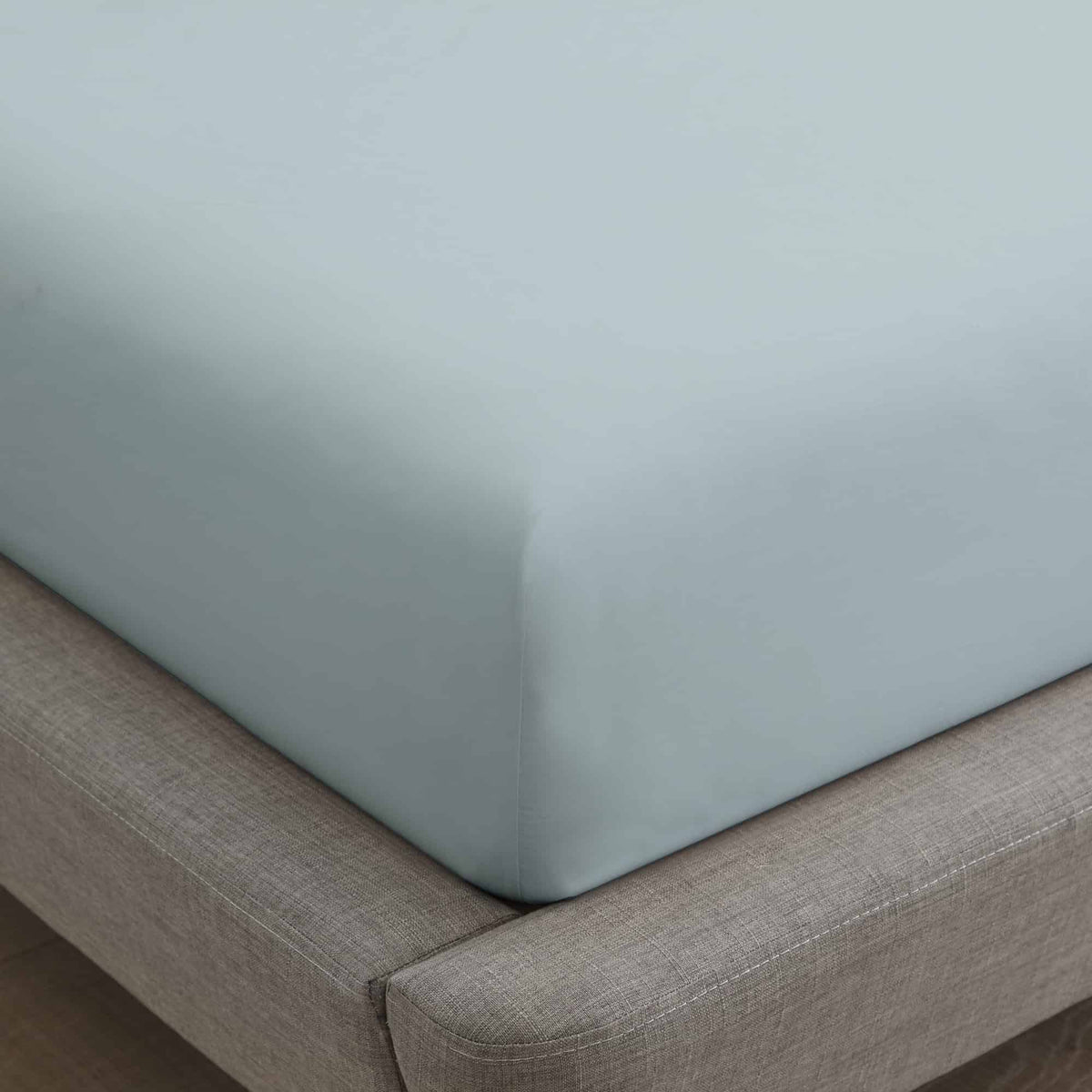 Soft light blue fitted sheet stretched smoothly over mattress corner on grey frame