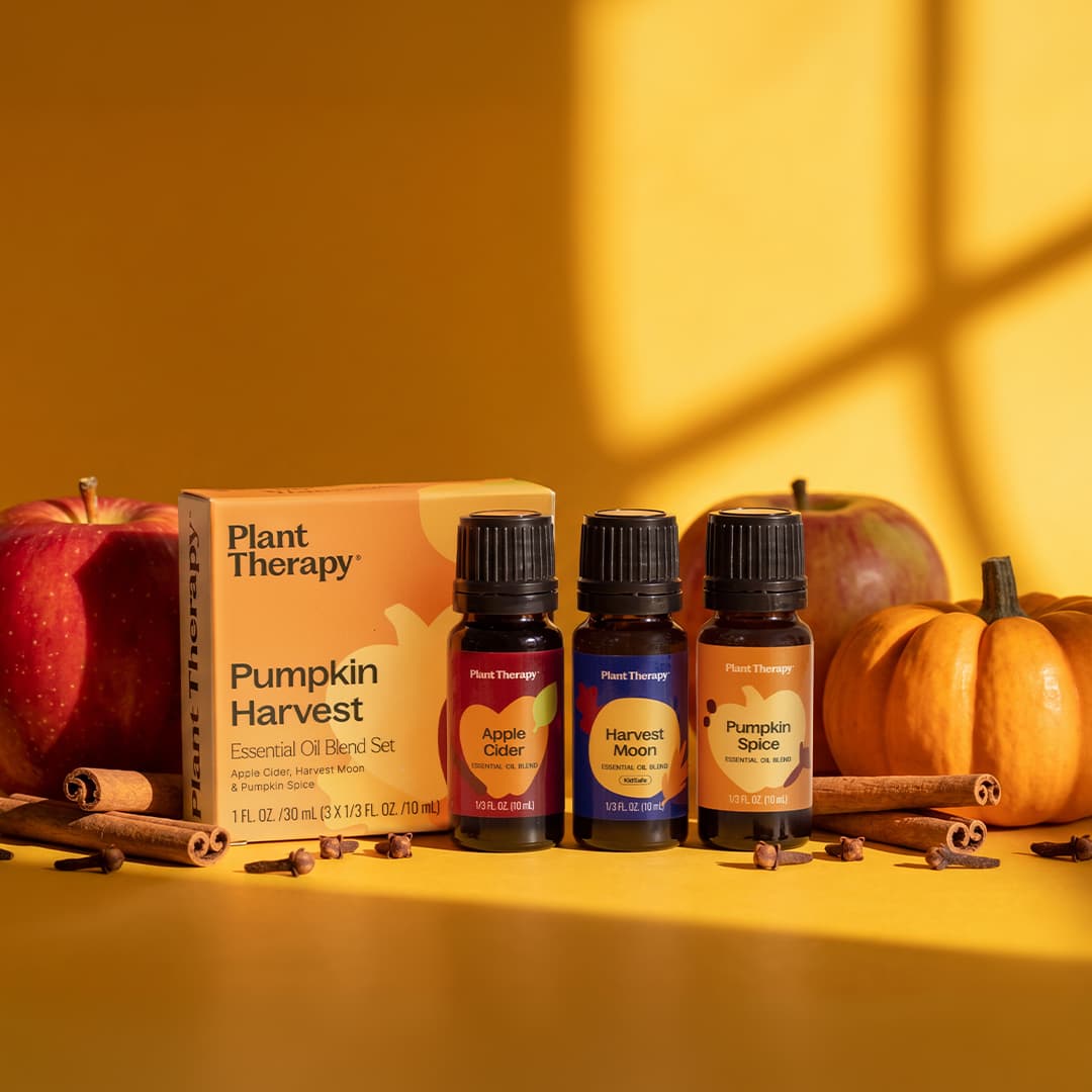 Pumpkin Harvest Essential Oil Set box and three bottles surrounded by red apples, mini pumpkins, and cinnamon sticks on a