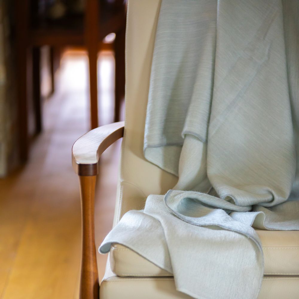 Light gray handwoven alpaca throw draped over cream leather chair arm