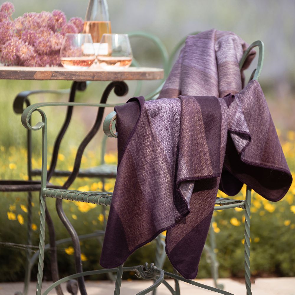 Deep purple and maroon striped alpaca throw draped over a green wrought-iron garden chair