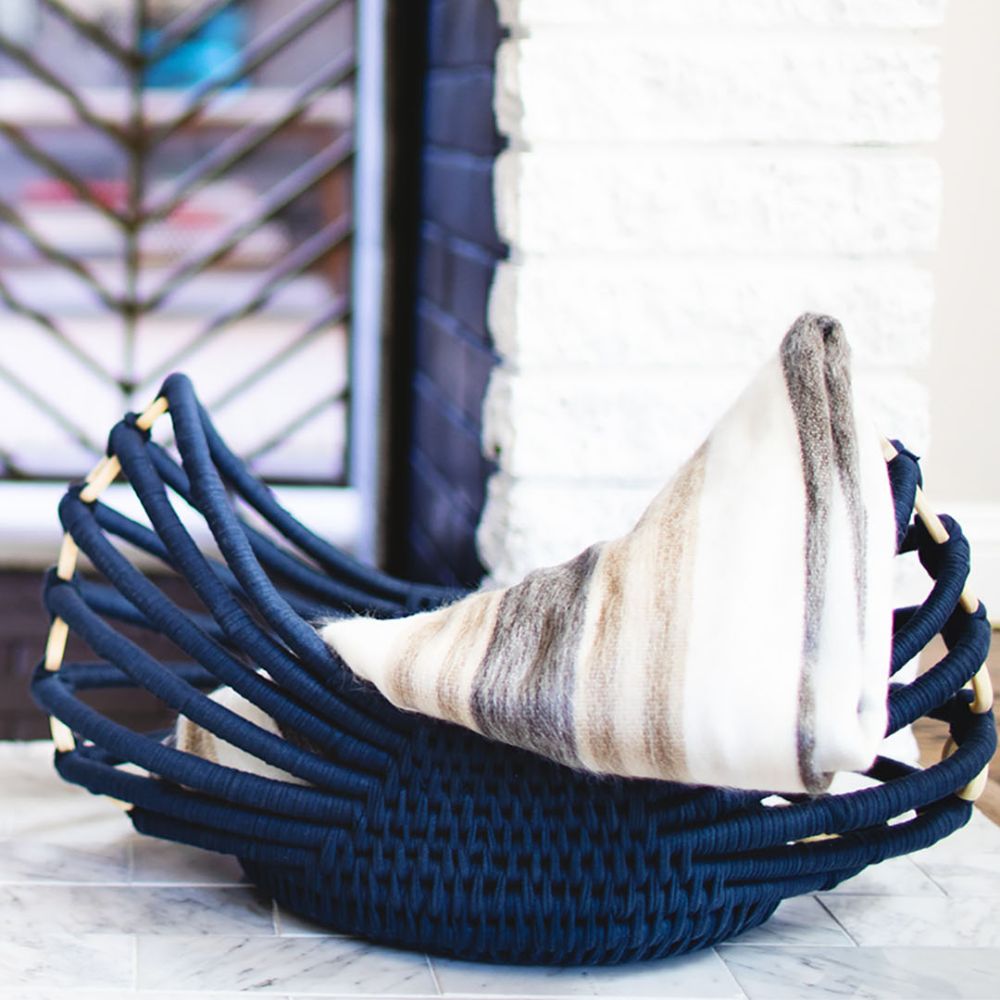 Folded alpaca blanket in navy rope basket by white fireplace