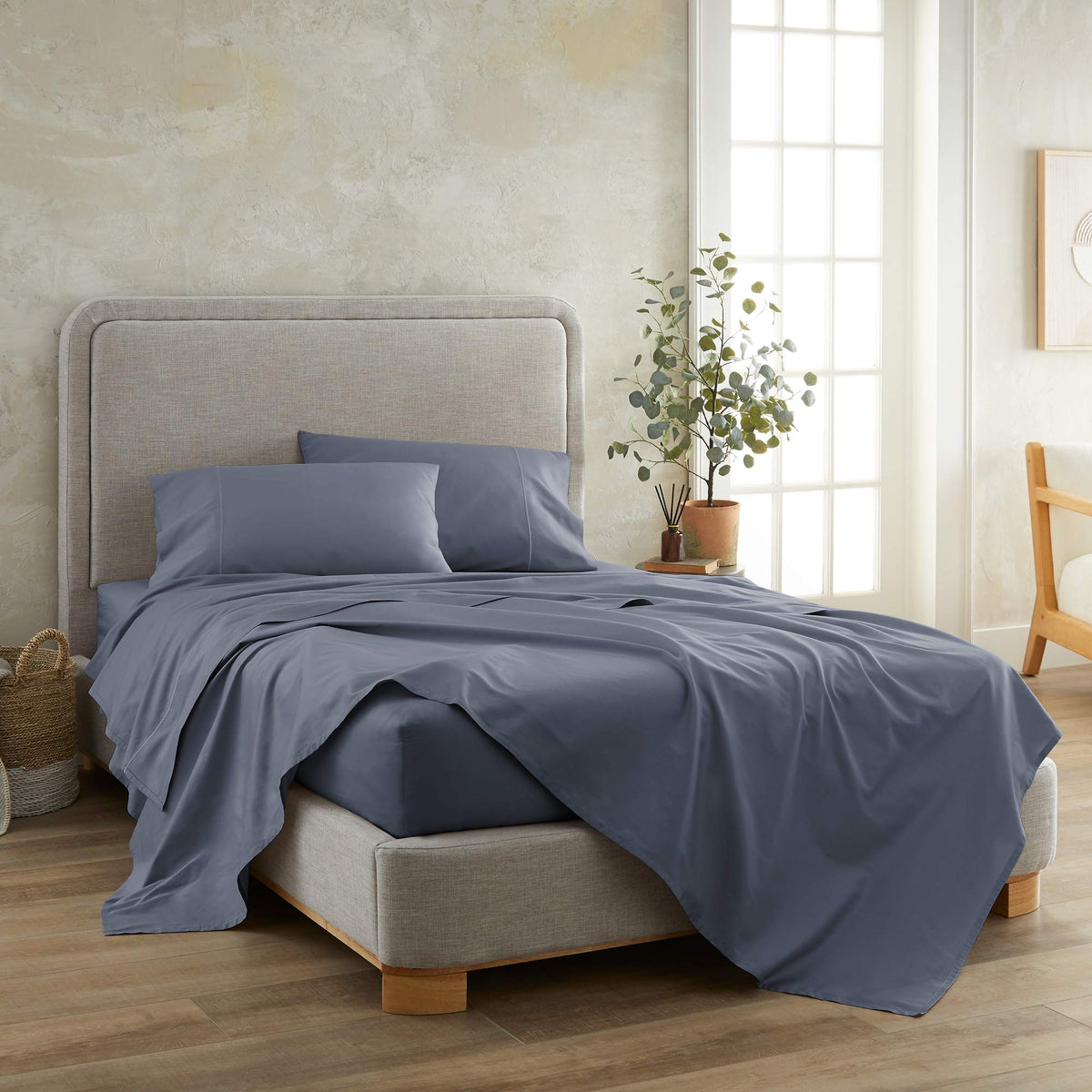 Slate blue 300 TC sateen sheet set with natural draping folds against textured beige wall