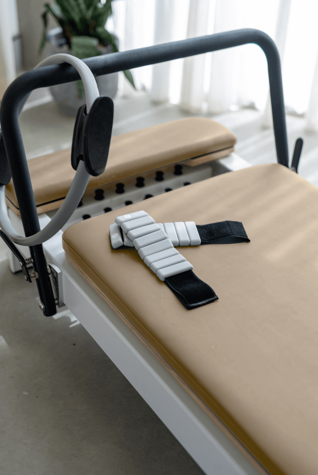 Beige reformer carriage with white segmented ankle strap and grey ring on black footbar