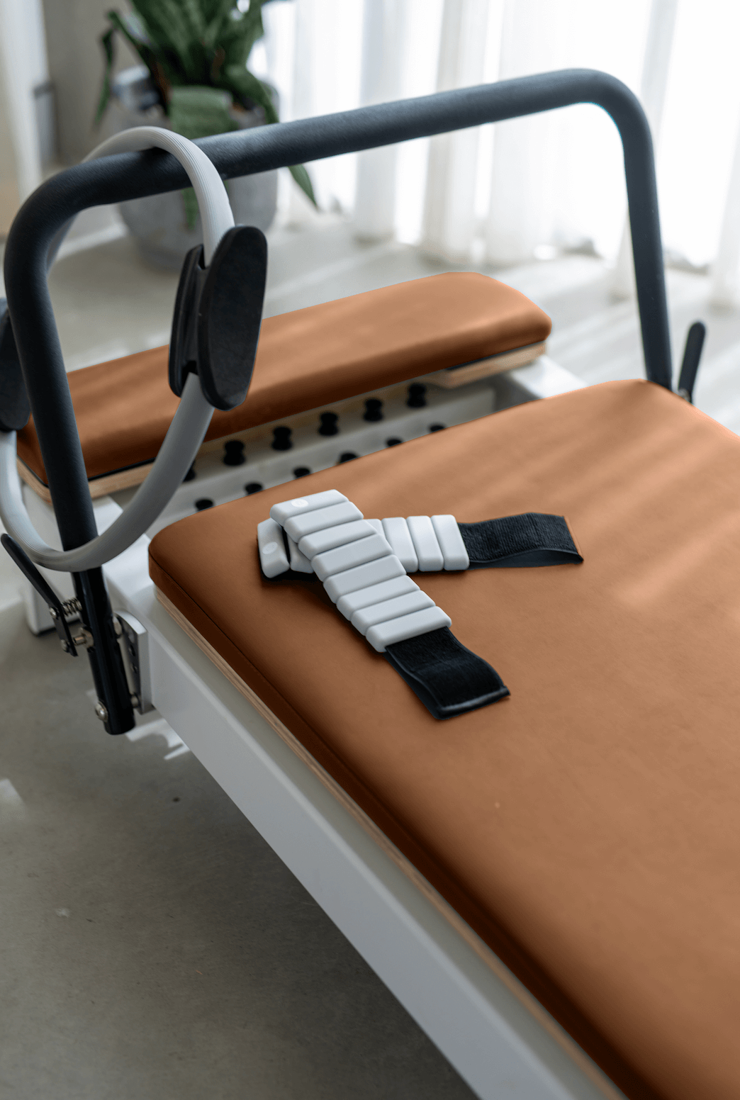 Terracotta orange reformer cushion detail with white segmented ankle strap on white frame