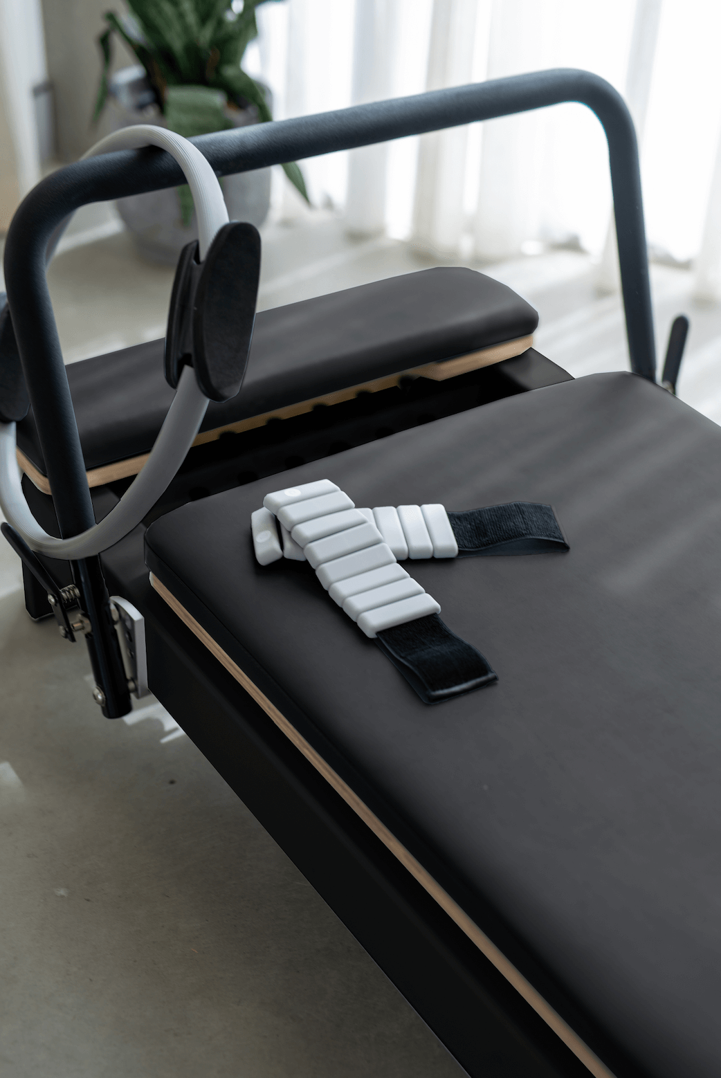 Close-up of black reformer carriage padding with grey resistance loop and white segmented ankle strap near window