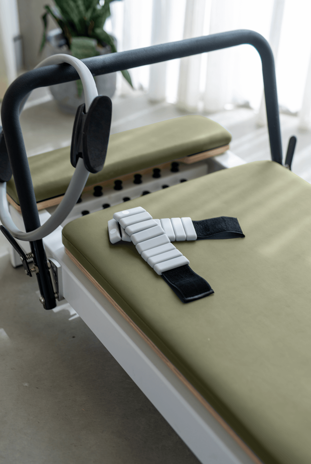 Olive green reformer carriage close-up showing fabric texture, ankle strap, and grey ring