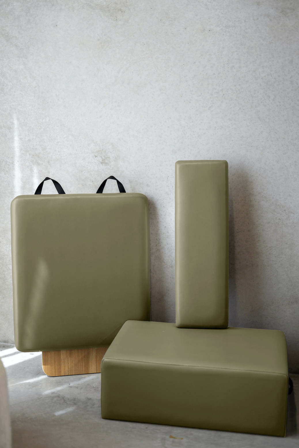 Sage green Pilates accessory set with box, standing platform, and jumpboard against textured concrete wall