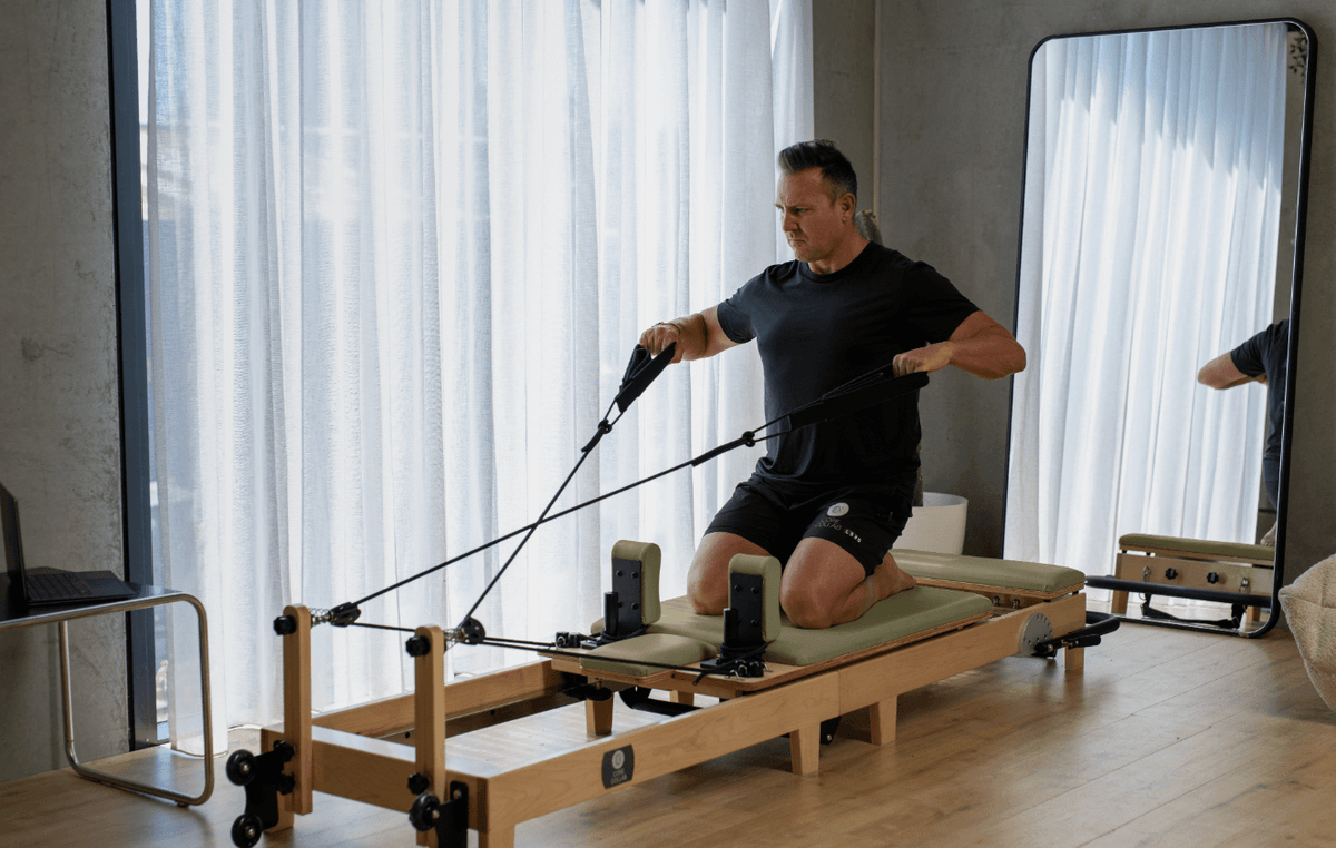 Man exercising on olive green reformer demonstrating stability in modern studio with mirrored walls