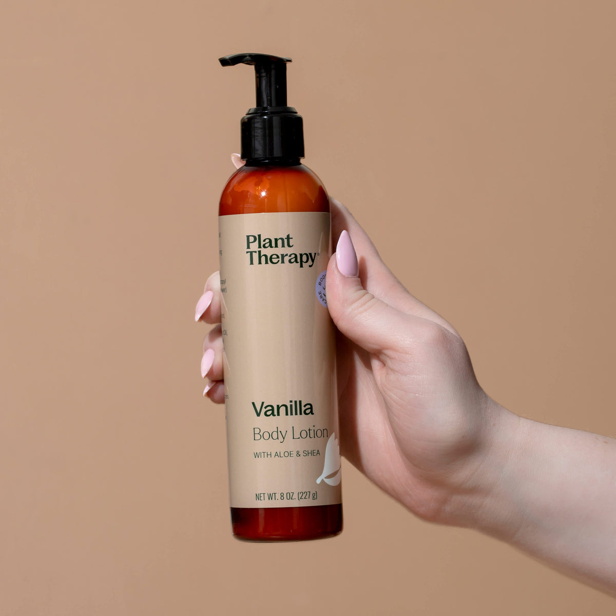 Hand holding amber pump lotion bottle showing front label against beige background
