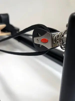 Macro view of high-tension pulley system with black braided rope threaded through polished silver mechanism and red safety