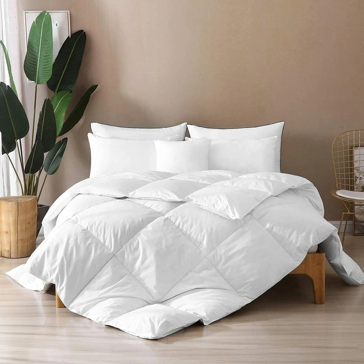 Fluffy white bamboo-viscose comforter stacked with pillows on a bed against a beige wall, next to a green plant and gold