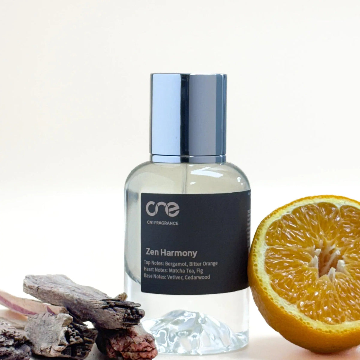 Cylindrical glass Zen Harmony bottle with silver cap and black label beside orange slice and driftwood
