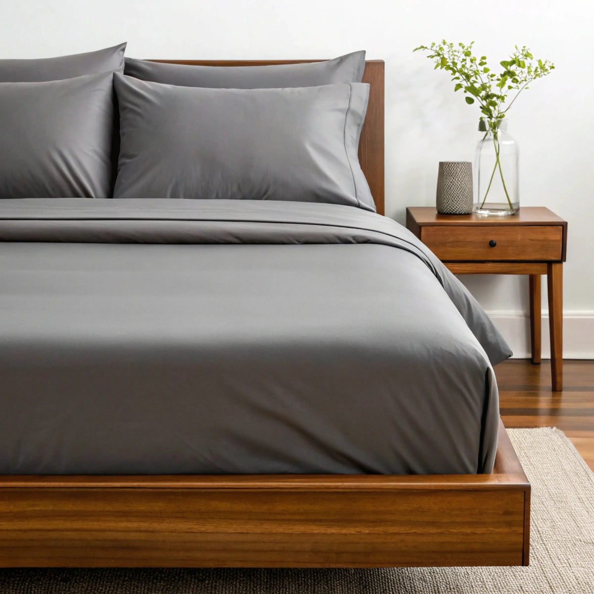 Side angle showing deep fit of dark grey fitted sheet around mattress corner with stacked pillows against wooden headboard