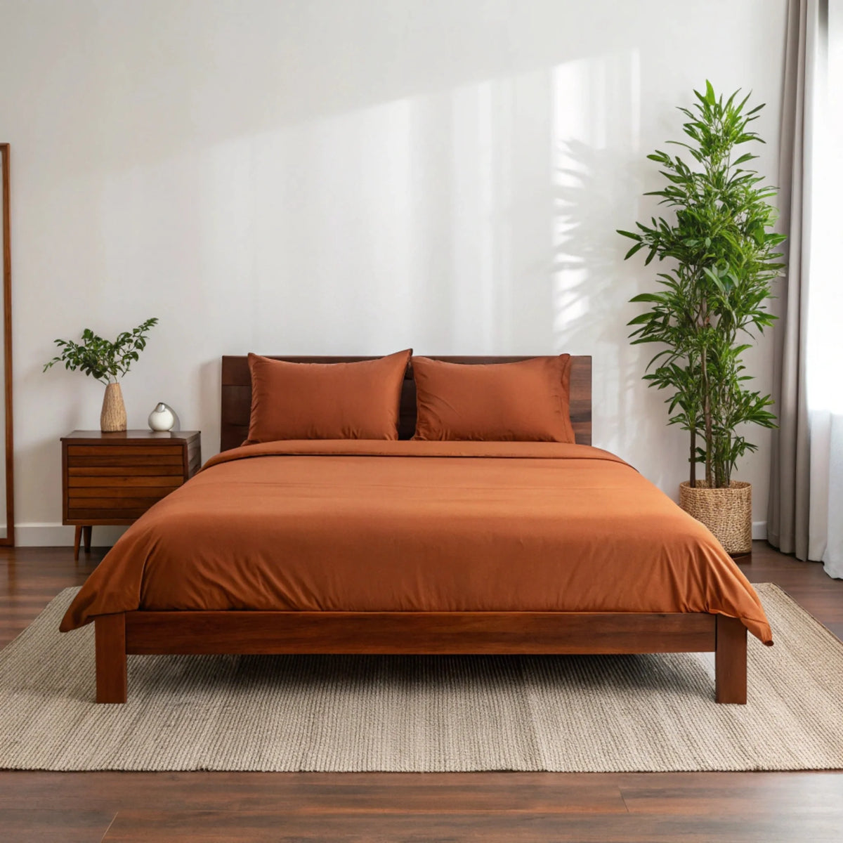 Wide shot of terracotta orange sheets contrasting with dark wood frame, accompanied by tall potted plant and warm lighting