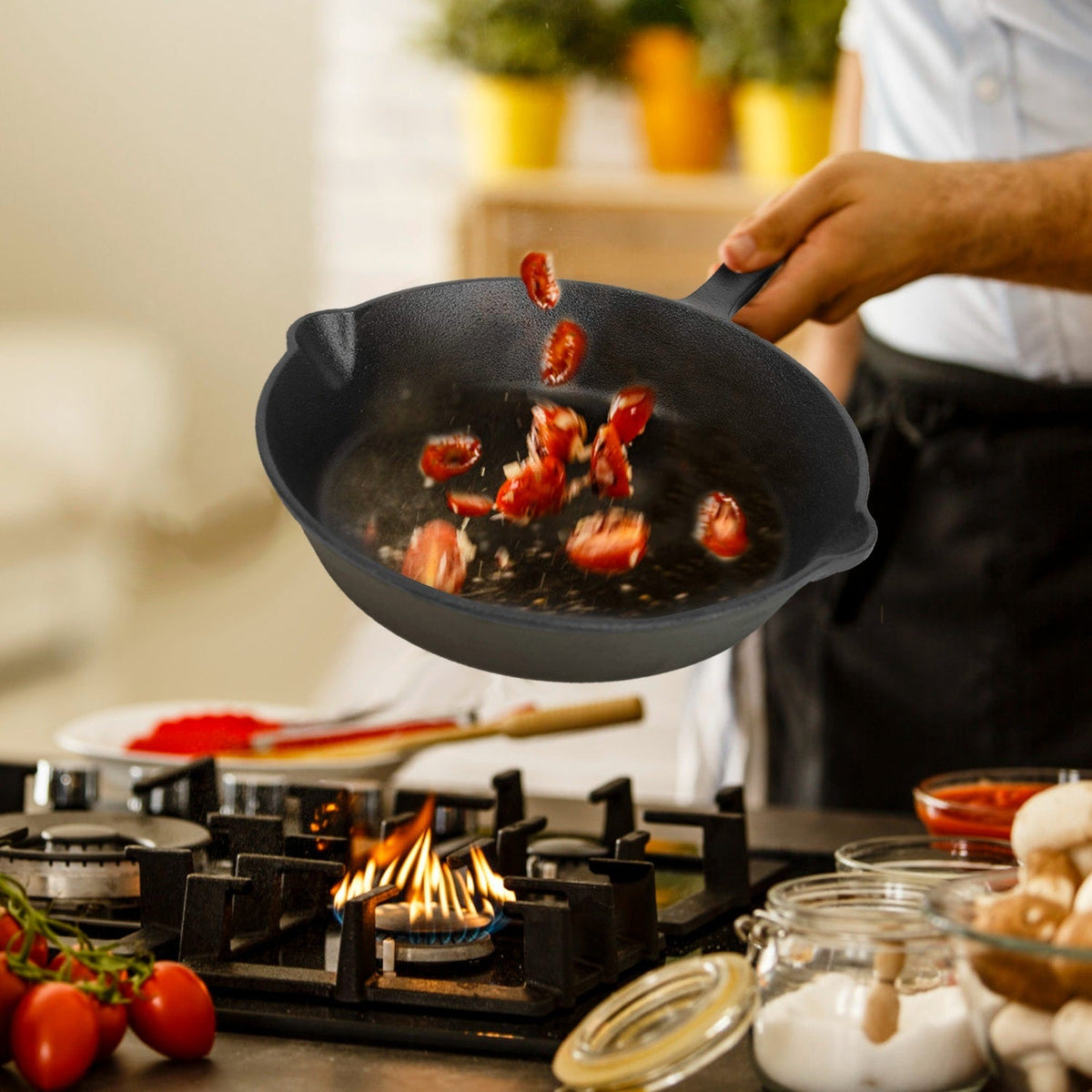 Person tossing cherry tomatoes in small black cast iron skillet over lit gas stove burner flame